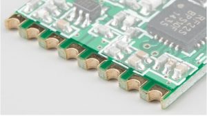 Close-up of PCB with castellated via edges, showing exposed copper plating on half-cut vias for surface-mount assembly.
