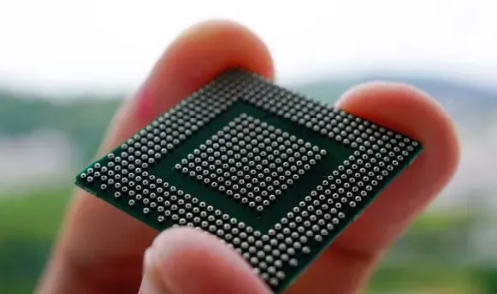 Close-up of a BGA packaged chip held in hand, showing the dense array of solder balls on the bottom surface.