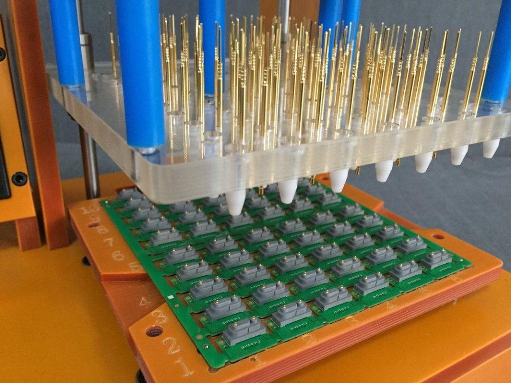 PCB test jig with precision spring probe pins descending to contact PCBA, automated electrical continuity testing fixture for mass production.