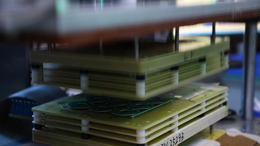 Stacked multi-layer PCB functional test fixture, upper jig plate pressing down on circuit board for automated function verification.